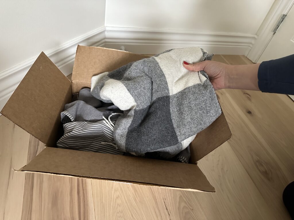 a hand decluttering a grey scarf into a cardboard box