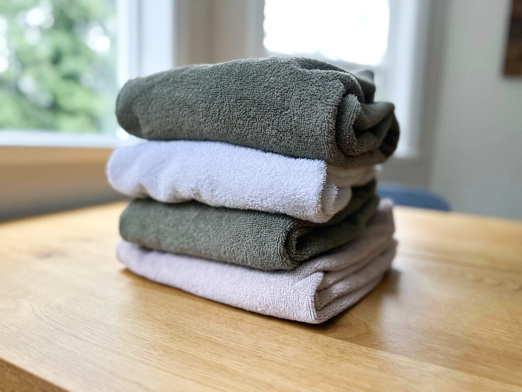 an off white towel, two green towels and a white town on a white towel. Keep the towels you like when you organize your linens