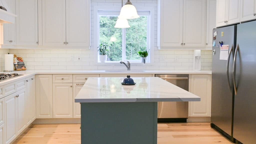 tidy decluttered minimalist kitchen with white cupboards and countertops and a greenish blue island