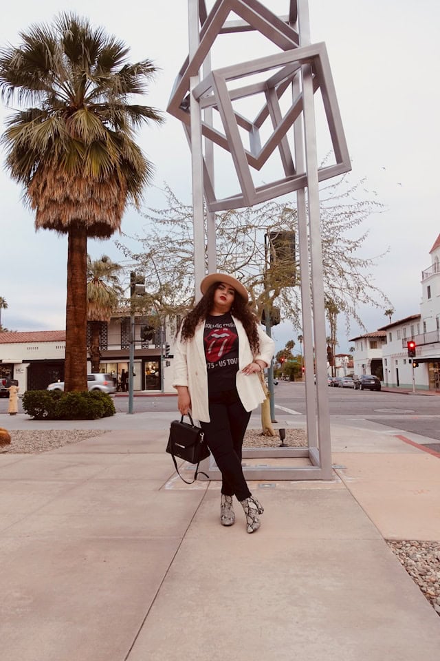 Lady standing with white coat, black purse and brown hat