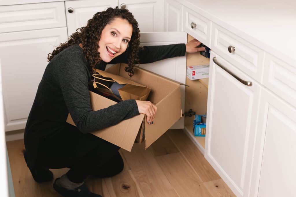 woman holding a box, decluttering and reaching into a cupboard
