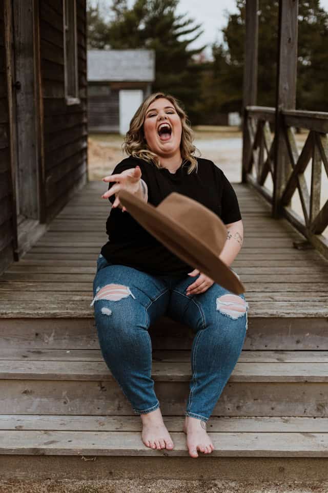 lady sitting with black top, jeans and throwing a hat