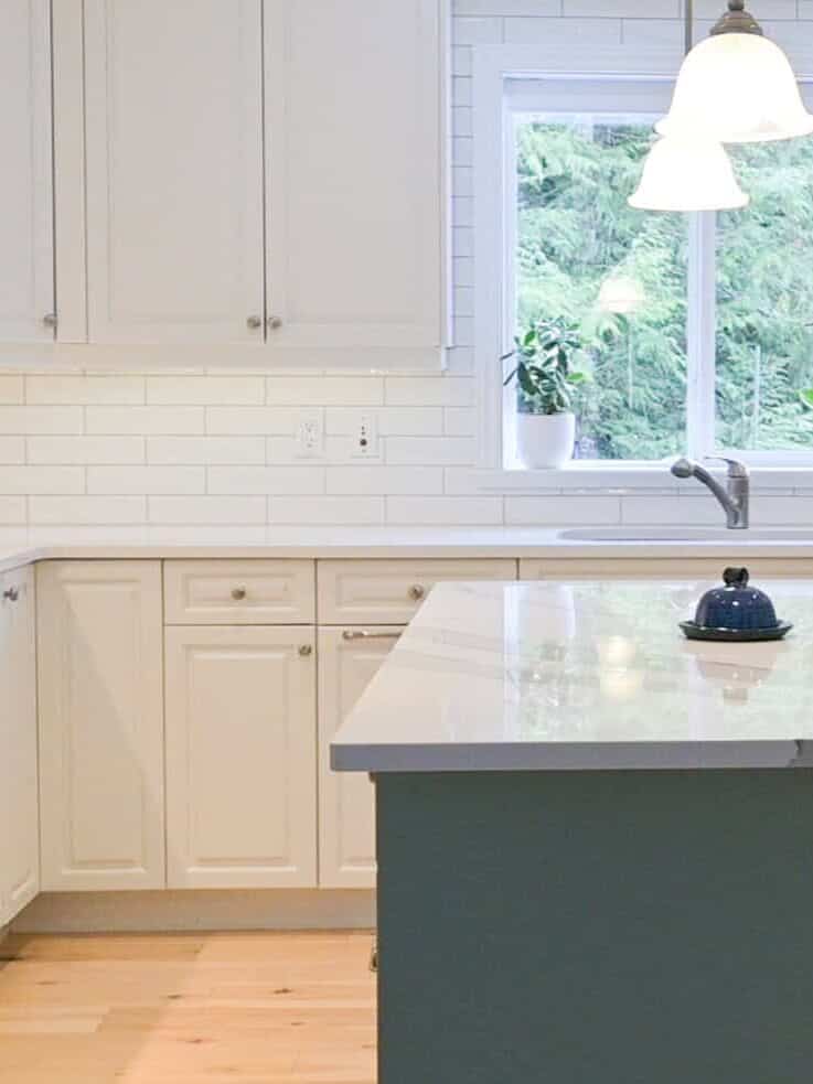 tidy decluttered minimalist kitchen with white cupboards and countertops and a greenish blue island