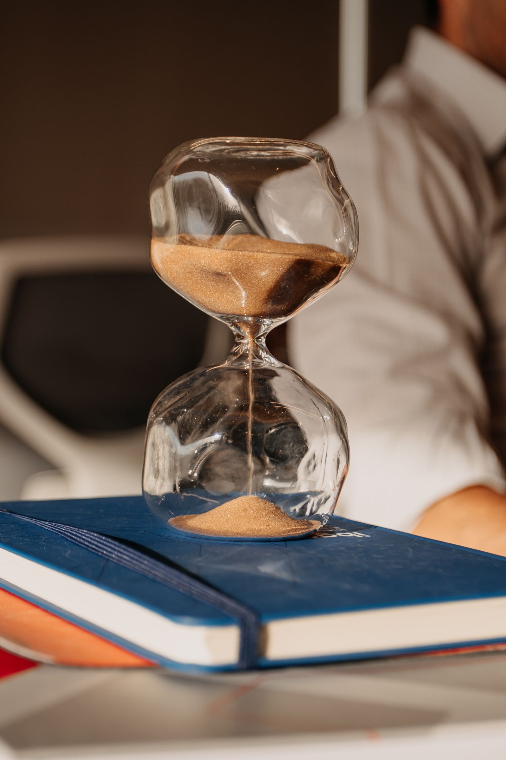 A glass hourglass with sand on books in a modern office environment.. PEXELS