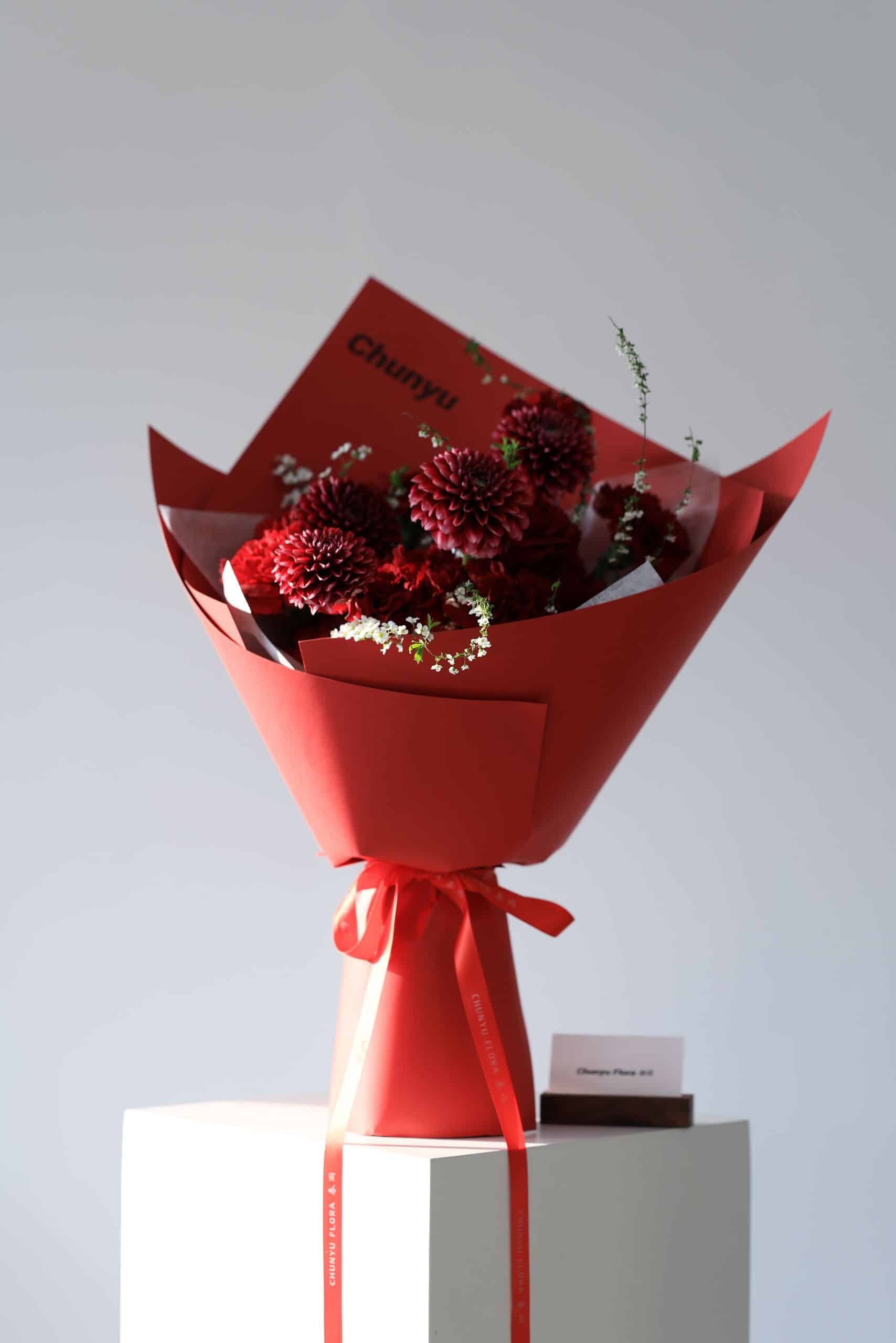 A striking red dahlia bouquet wrapped in red paper with delicate white accents, perfect for gifting.