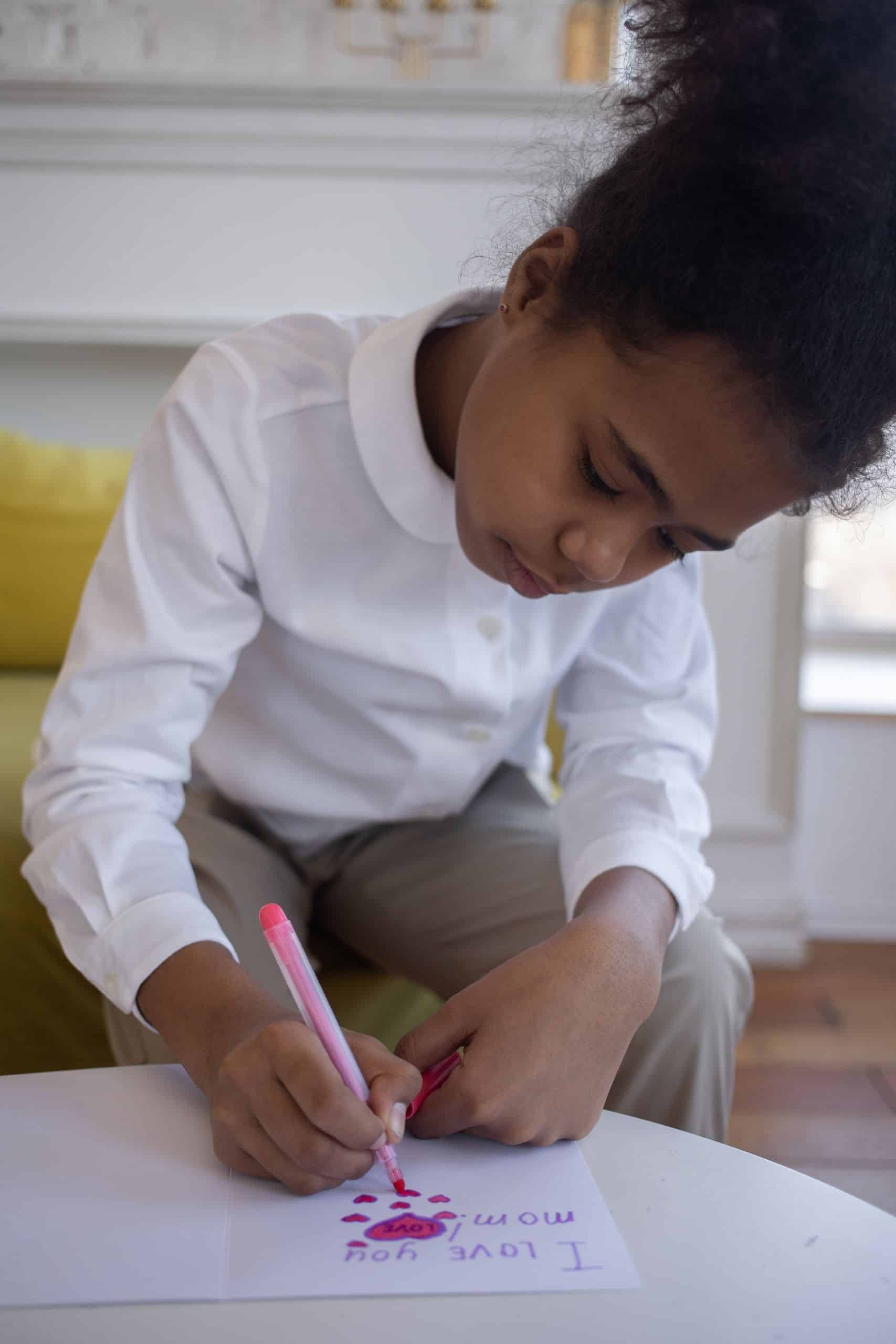 A young girl focuses intently while drawing with a pink marker in a cozy indoor setting.
