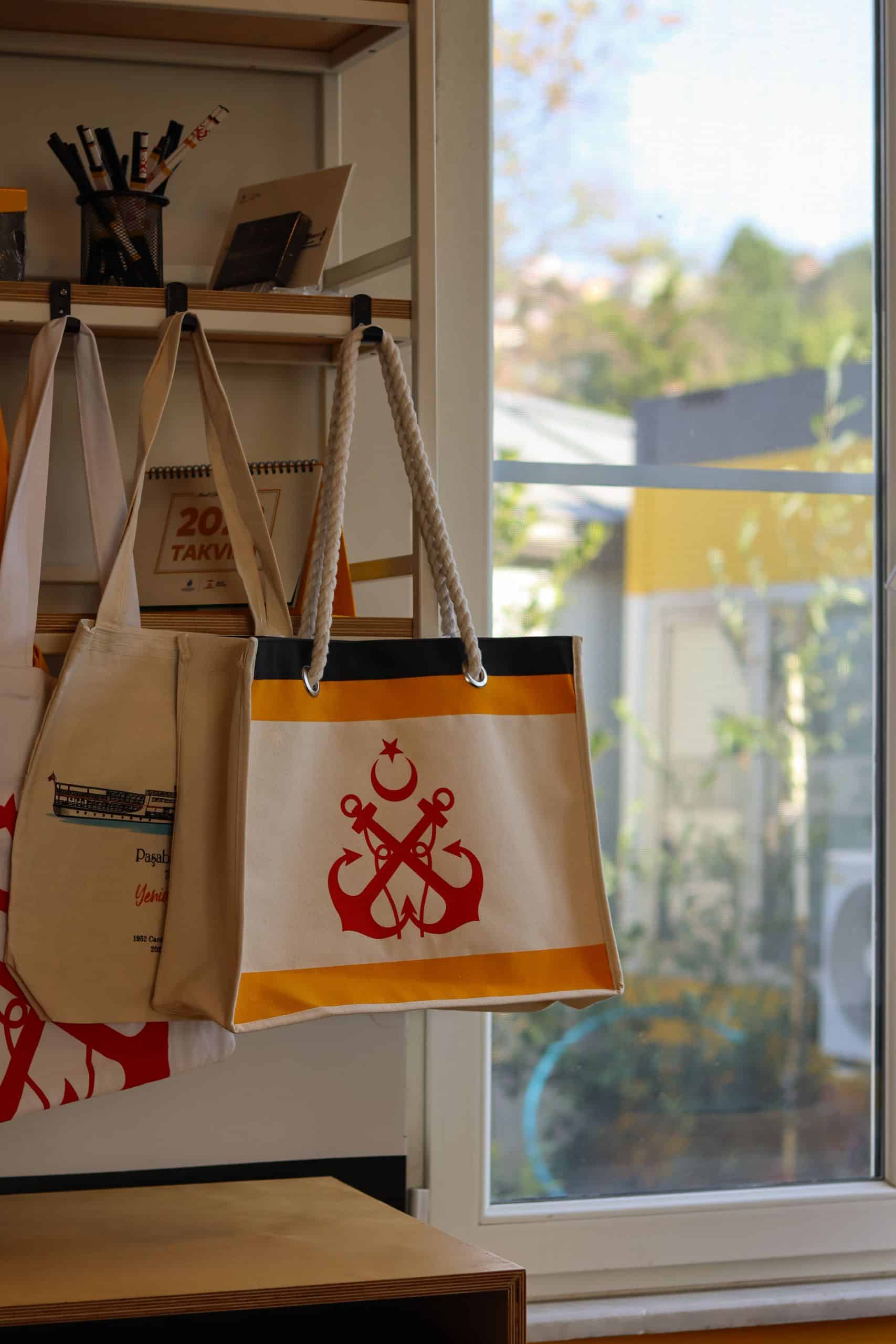 Canvas tote bags with anchor design hanging by a window in a sunlit room. Pexels