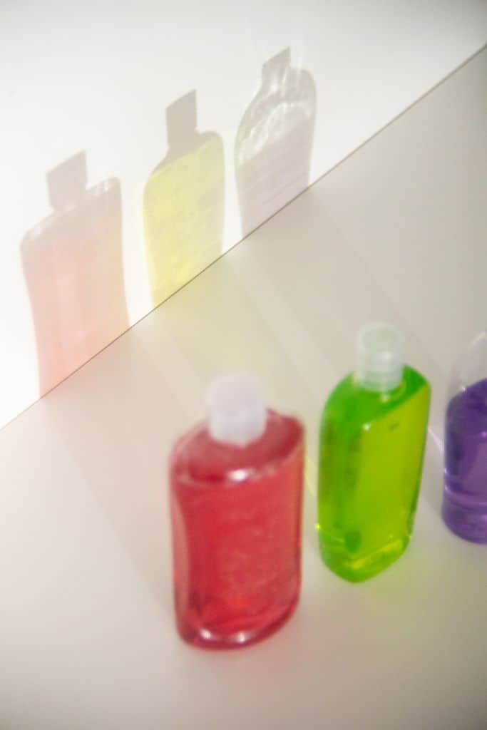 From above of assorted plastic bottles with colorful gels in row reflecting on white wall