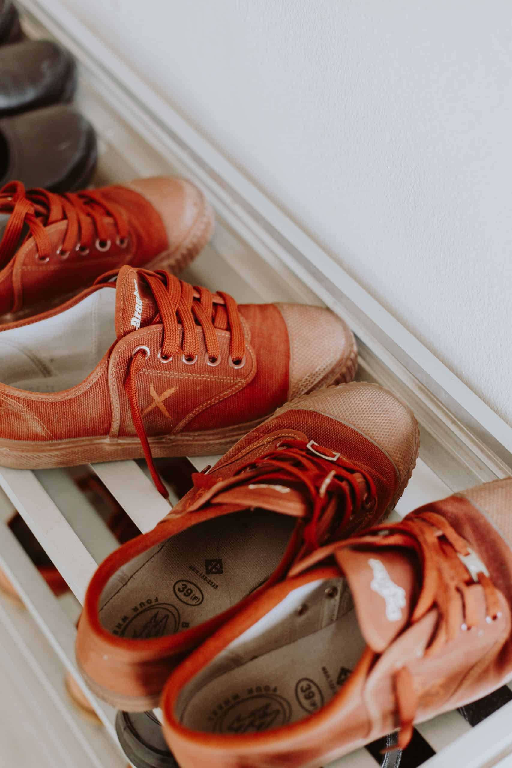 Rusty red sneakers organized neatly on a sleek white shoe rack indoors.