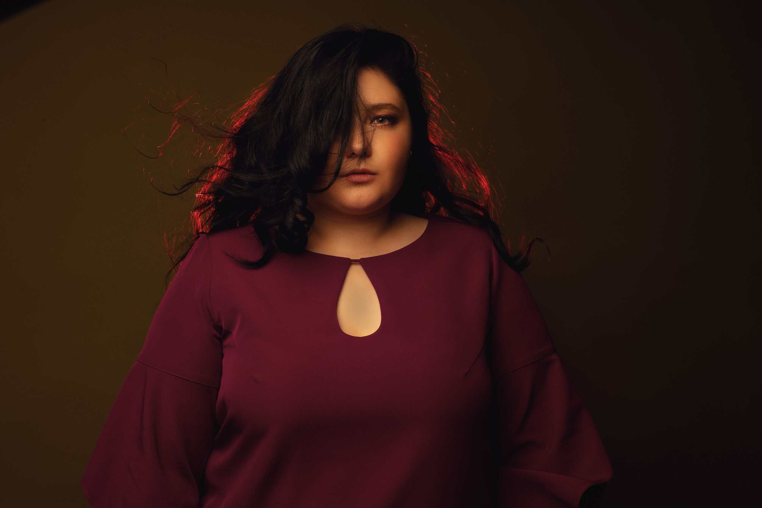 Studio portrait of a plus-size woman in a maroon shirt with stylish lighting and brown background.