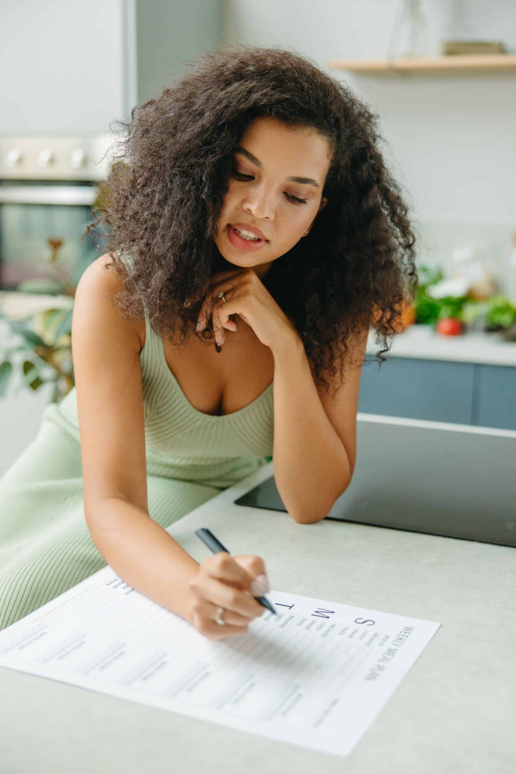 Young woman with curly hair planning a healthy meal indoors. Focus on meal planning and lifestyle. pexels