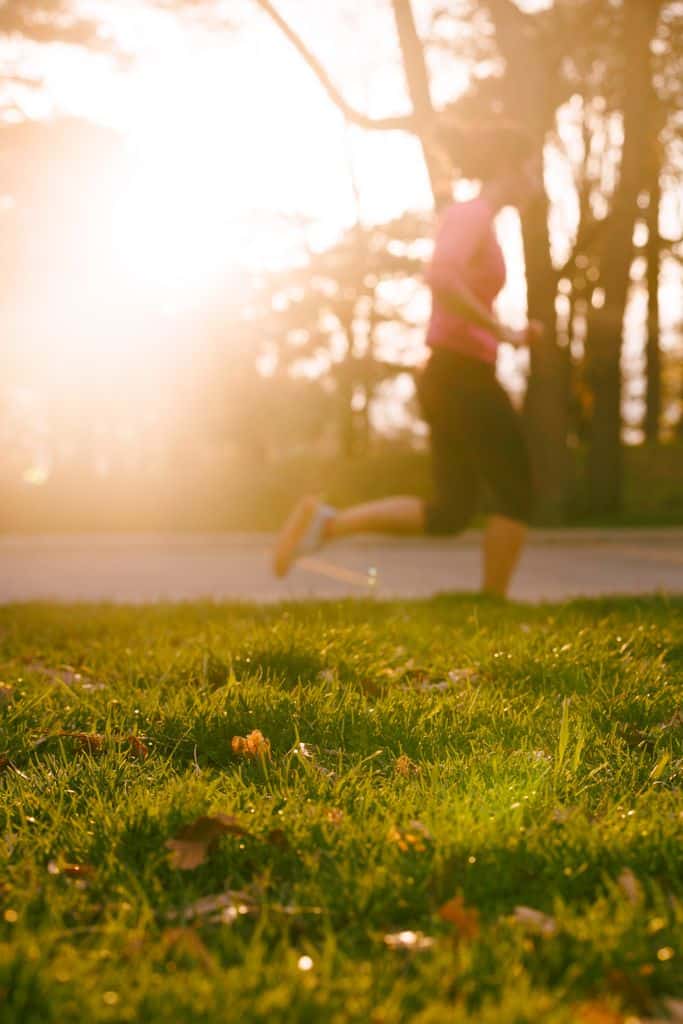 A woman jogging through a sunlit park during sunrise, embodying wellness and vitality.